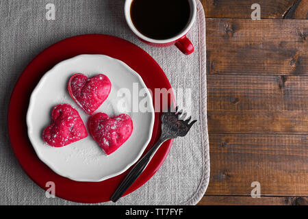Cookies in Form von Herzen in der Platte mit Tasse Kaffee auf Serviette, auf rustikalen hölzernen Planken Hintergrund Stockfoto
