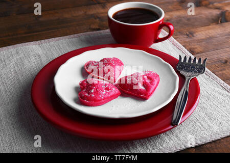 Cookies in Form von Herzen in der Platte mit Tasse Kaffee auf Serviette, auf rustikalen hölzernen Planken Hintergrund Stockfoto
