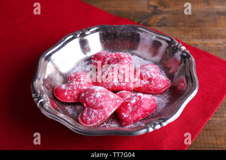 Cookies in Form von Herzen auf Metall Fach und Serviette auf hölzernen Tisch Hintergrund Stockfoto