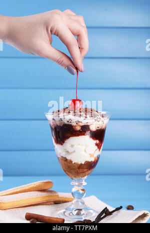 Hand, die Kirsche oben leckeres Tiramisu Dessert im Glas, in Farbe Holz- Hintergrund Stockfoto