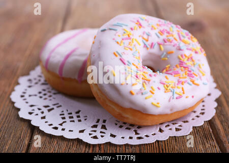 Delicious Doughnuts mit Zuckerglasur auf Spitze Deckchen auf hölzernen Hintergrund Stockfoto