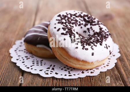 Delicious Doughnuts mit Zuckerglasur auf Spitze Deckchen auf hölzernen Hintergrund Stockfoto