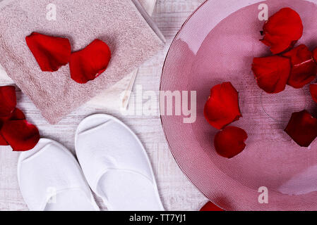 Spa Schüssel mit Wasser, Rosenblüten, Handtuch und Badeschuhe auf hellen Hintergrund. Konzept der Pediküre oder Natural Spa Behandlung Stockfoto