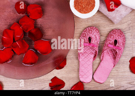 Spa Schüssel mit Wasser, Rosenblüten, Handtuch und Badeschuhe auf hellen Hintergrund. Konzept der Pediküre oder Natural Spa Behandlung Stockfoto