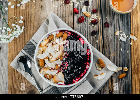 Eine Schüssel Haferbrei schön mit Nüssen, Mandeln und Preiselbeeren auf einem hölzernen Tisch dekoriert Stockfoto