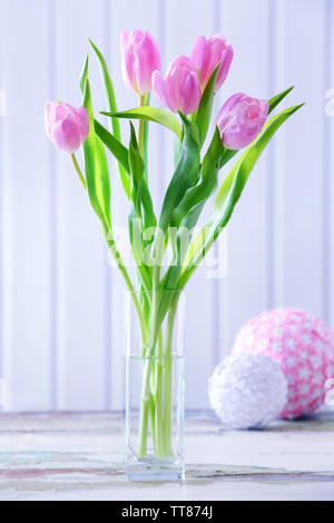 Schöne rosa Tulpen in der Vase mit dekorativen Kugeln auf dem Tisch auf hölzernen Hintergrund Stockfoto