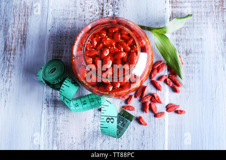 Goji Beeren in Glasschale mit Maßband und Blätter auf Farbe holztisch Hintergrund Stockfoto