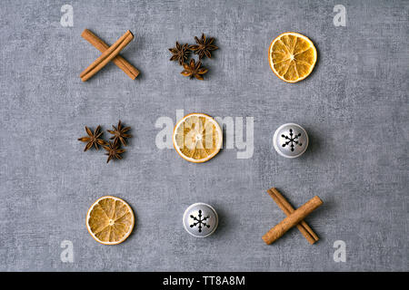 Weihnachten Nullen und Kreuze deco mit getrockneten Orangen, cinamon aniseeds, Sticks und silbernen Glocken auf grauem Hintergrund Stockfoto