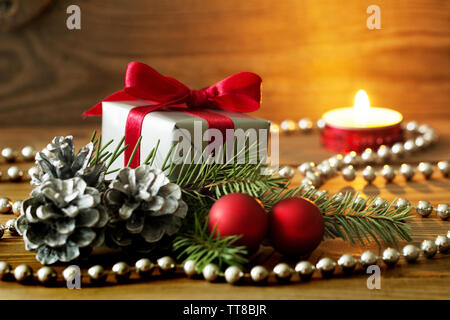 Weihnachten Zusammensetzung: ein Geschenk mit roter Schleife silber Kegel, rote Kugeln und ein Fir Tree Branch - brennende Kerze im Hintergrund gewickelt Stockfoto