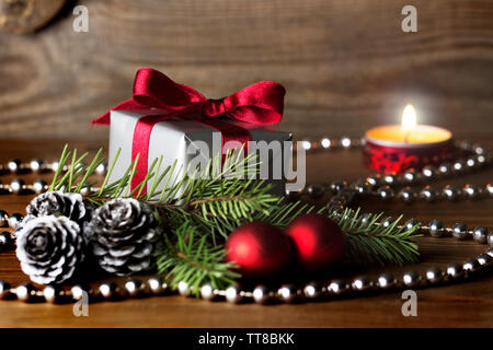 Weihnachten Zusammensetzung: ein Geschenk mit roter Schleife silber Kegel, rote Kugeln und ein Fir Tree Branch - brennende Kerze im Hintergrund gewickelt Stockfoto