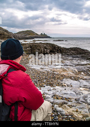 Ein Wanderer sitzt und bewundert die Ansicht von Armband Bay Beach. Der Leuchtturm auf Mumbles Mumbles Head kann von hier aus gesehen werden. Swansea, Gower, Wales, UK. Stockfoto