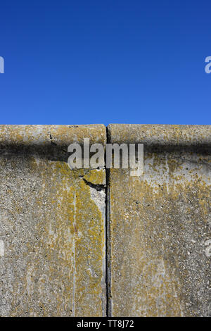 Beschädigte Betonfertigteilmauer, Riss am Ausdehnungsgelenk, Algenwachstum, in klarem blauen Himmel und keine Wolken an der Rossall-Küste in Lancashire uk Stockfoto