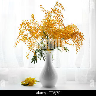 Schöne Zweige von Mimosa in Vase auf Fensterbank Stockfoto