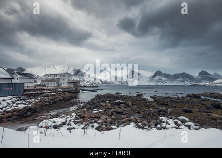 Snowy Mountain Range mit stürmischen Himmel im Fischerdorf an der Küste im Winter bei Mefjord Brygge Stockfoto