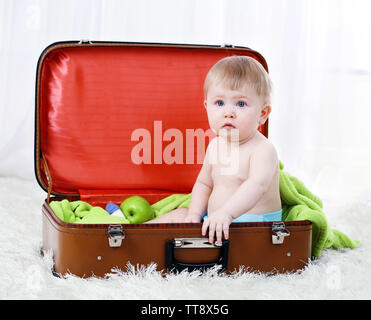 Cute Baby boy in großen Koffer sitzen auf dem Teppich, auf hellen Hintergrund Stockfoto