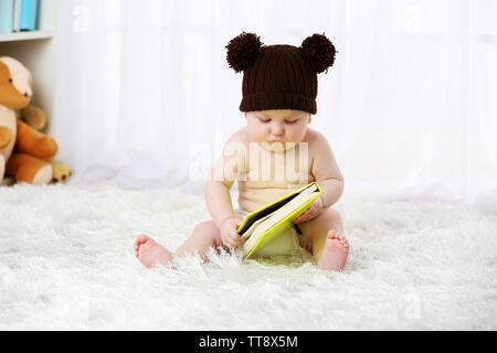 Cute Baby boy in lustige Kappe sitzt auf Teppich mit Notebook, auf hellen Hintergrund Stockfoto