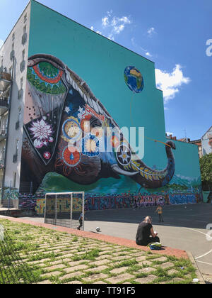 Berlin, Deutschland - Juni 2019: Kinder spielen im Freien auf Fußball Spielplatz auf der Straße mit Graffiti Wandbild im Hintergrund in Berlin Kreuzberg Stockfoto