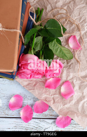 Schöne rosa Rosen mit Stapel von Büchern auf Holztisch mit Pergament, Ansicht von oben Stockfoto