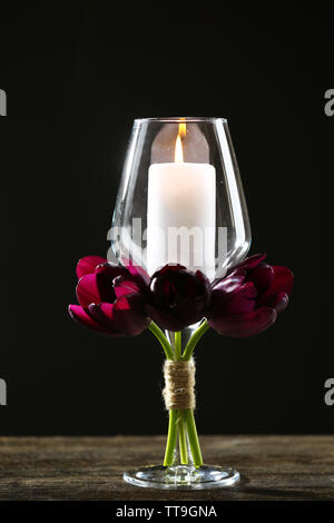 Stillleben mit Kerze im Glas und lila Tulpen auf schwarzem Hintergrund Stockfoto