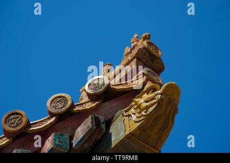 Zu den Tieren auf die Ecken der traditionellen chinesischen Dächer geschnitzt - gelb und rosa Artwork vor einem strahlend blauen Himmel Stockfoto