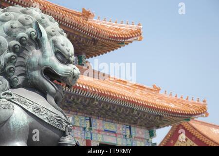 Eine Statue eines knurrenden Chinesischer Drache (Lion) im Vordergrund; teilweise de-gesättigtes Bild eines traditionellen chinesischen Gebäude im Hintergrund - Bri Stockfoto