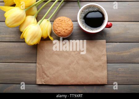 Tasse Kaffee mit frischen Kuchen, Tulpen und leeres Blatt Papier auf Holz- Hintergrund Stockfoto