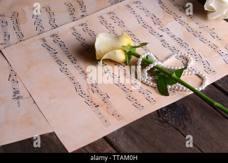 Schöne Rose mit Perlen auf Musik Blätter auf Holztisch, Nahaufnahme Stockfoto