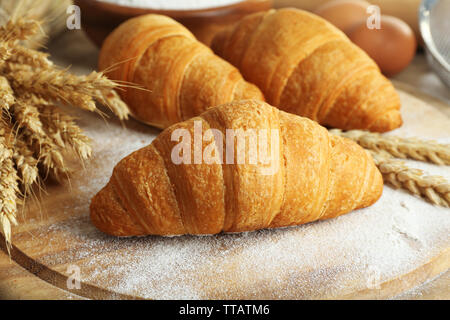 Frische Croissants mit Mehl auf Holztisch, Nahaufnahme Stockfoto