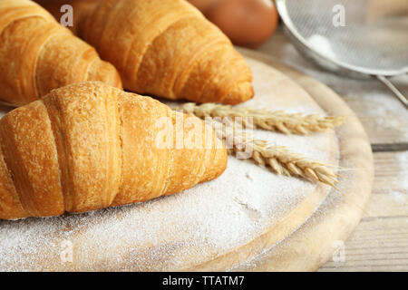 Frische Croissants mit Mehl auf Holztisch, Nahaufnahme Stockfoto