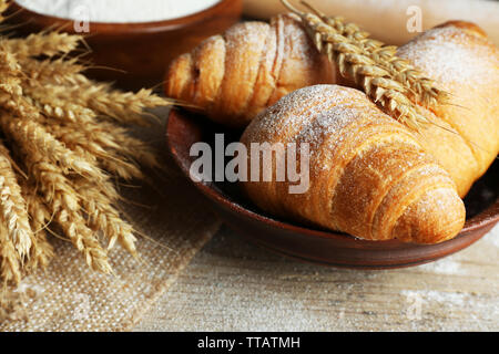 Frische Croissants mit Mehl auf Holztisch, Nahaufnahme Stockfoto