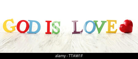 Gott ist die Liebe mit bunten Kunststoff Holz Buchstaben auf weißem Hintergrund dargestellt Stockfoto