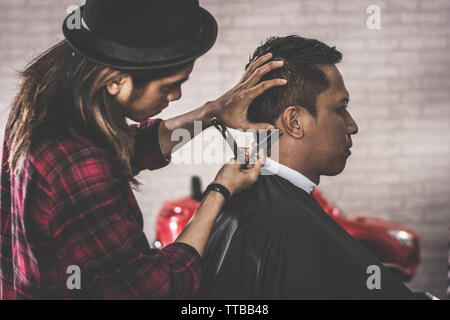 Nahaufnahme Portrait von asiatischen Friseur mit langem Haar rasieren seinen Kunden Haar an barbershop Stuhl Stockfoto