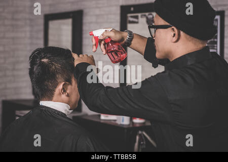 Rückspiegel der Friseur- oder Friseur besprüht Wassers mit dem Spray auf das Haar der Client in einem Vintage barbershop mit der rechten Hand, Stockfoto