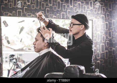 Portrait von professionellen Friseur die Haare schneiden seiner attraktiven Mann Kunde mit Schere und Kamm in Vintage barbershop Stockfoto