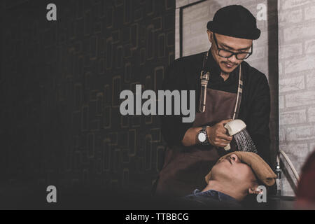 Portrait von Friseur wäscht costumer Haar mit Strom Wasser Dusche, die sich in den Stuhl sinken entspannt mit frischem Handtuch in Vintage barbershop Stockfoto