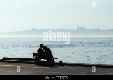 Istanbul, Türkei - 12. Juni, 2019: Junge Liebhaber sitzen und küssen auf einer Bank vor der nebligen Istanbul Landschaft. Stockfoto