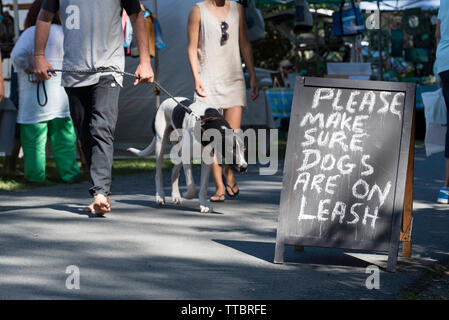 Leute und ein Hund an einem Wochenende Landwirt Markt der Gemeinschaft bei Pacific Palms, New South Wales mit einem Schild bittet die Besitzer ihren Hund an der Leine zu halten. Stockfoto