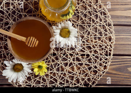Honig im Topf und in der Schüssel, Pendelarm und Blumen auf wicker Matte auf Holz- Hintergrund Stockfoto