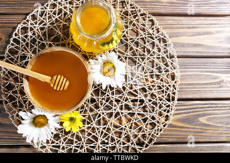 Honig im Topf und in der Schüssel, Pendelarm und Blumen auf wicker Matte auf Holz- Hintergrund Stockfoto