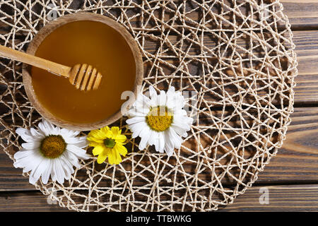 Honig im Topf und in der Schüssel, Pendelarm und Blumen auf wicker Matte auf Holz- Hintergrund Stockfoto