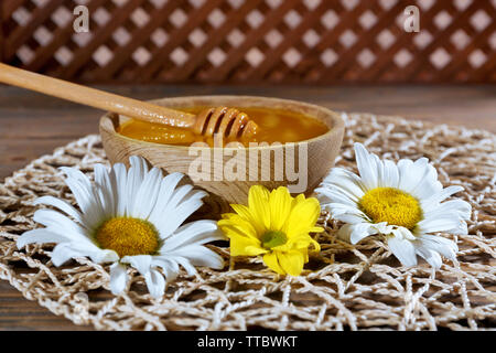 Schüssel mit Honig mit hölzernen Pendelarm und Blumen auf wicker Mat closeup Stockfoto