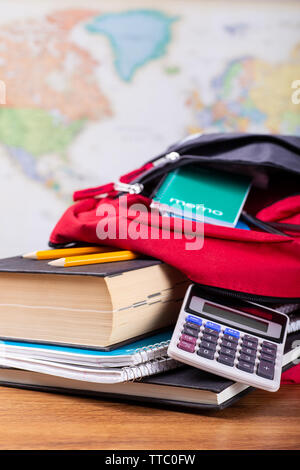 Nahaufnahme der einen Rucksack mit Schule Elemente auf einem Schreibtisch mit Weltkarte im Hintergrund Stockfoto