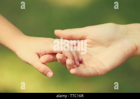 Die Mutter von Hand führen ihr Kind Tochter im Freien auf Grün defokussiertem Hintergrund, vertrauen Familie Konzept Stockfoto