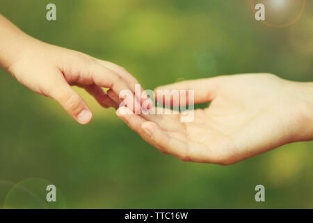 Die Mutter von Hand führen ihr Kind Tochter im Freien auf Grün defokussiertem Hintergrund, vertrauen Familie Konzept Stockfoto