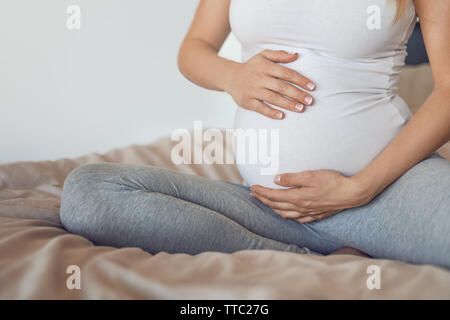 Junge schwangere Frau mit Ihrem Babybauch oder Bauch mit Ihren Händen in einer Nahaufnahme 7/8 Ansicht konzeptionelle der mütterlichen Liebe Stockfoto