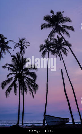 Silhouetten von Palmen gegen ein Sonnenuntergang über dem Meer mit einem Boot im Vordergrund. Stockfoto