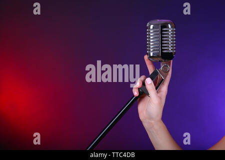 Weibliche hand mit einem retro Mikrofon gegen farbigen Hintergrund Stockfoto