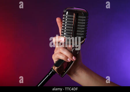 Weibliche hand mit einem retro Mikrofon gegen farbigen Hintergrund Stockfoto