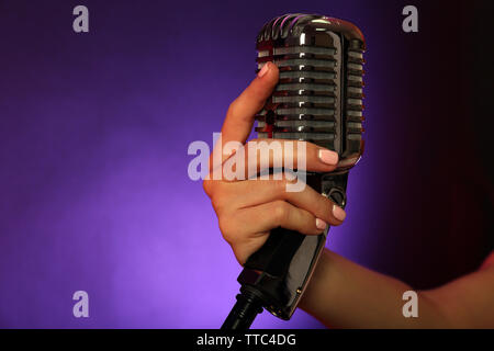 Weibliche hand mit einem retro Mikrofon gegen farbigen Hintergrund Stockfoto
