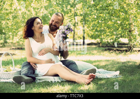 Schöner Mann gibt einen Blumenstrauß zu seinem schönen schwangere Frau im Park Stockfoto